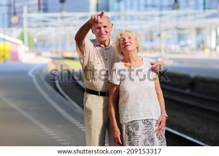 Happy senior caucasian couple travelling around Europe waiting for train in railway station platform in Amsterdam - active retirement concept