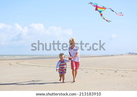 Happy children, teenager brother with cute toddler sister, playing together on the beach flying colorful kite