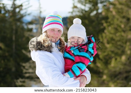 Happy young mother with cute toddler daughter in colorful snowsuit enjoying family vacation in snowy alpine village on a sunny winter day