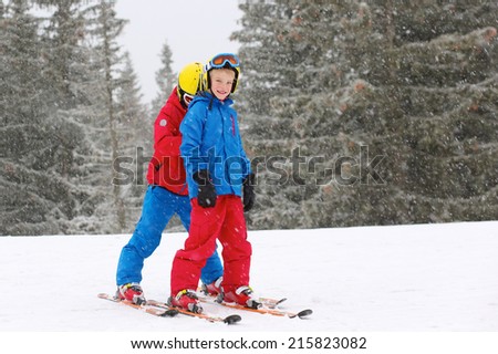 Two happy school  boys, twin brothers in colorful snowsuits, having fun skiing in alpine mountains during snowy winter vacation