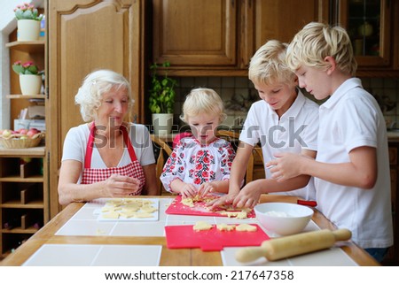 Loving caring grandmother, beautiful senior woman, baking tasty sweet cookies together with her grandchildren, cute little girl and two boys, sitting at the table in classic traditional wooden kitchen