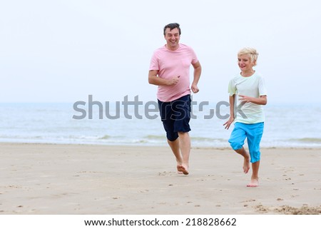 Father and son, cute blonde teenage boy, playing and running on wide sandy beach at the sea