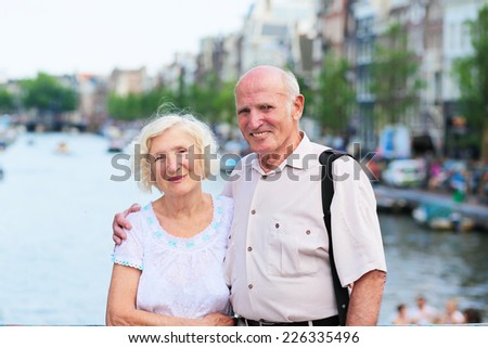 Happy senior caucasian couple traveling around Europe walking in the streets of Amsterdam, enjoying scenes of the canals on a sunny summer day - active retirement concept