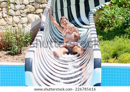 Happy family of two, young sportive mother and her little toddler daughter, having in water park enjoying big slide