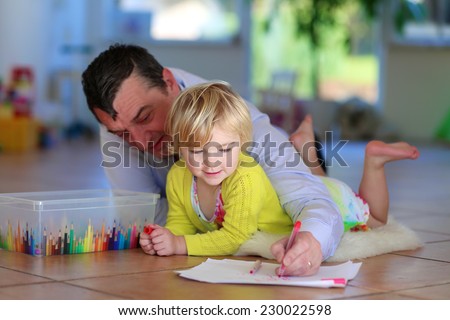 Happy family of two, loving caring father with child, adorable toddler girl, spending time together at home lying cozy on tiles floor on warm lambskin drawing picture with colorful felt-tip pencils