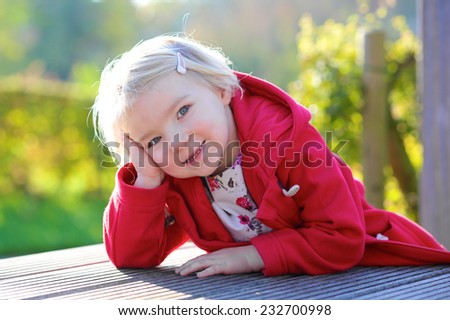 Portrait of beautiful little child, smiling blonde caucasian toddler girl in red duffle coat outdoors