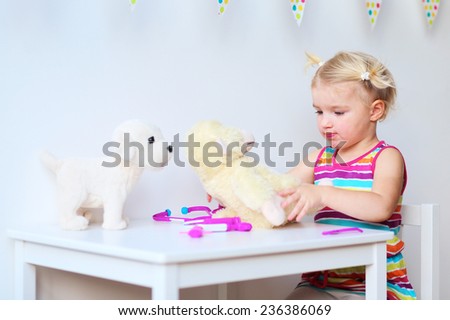 Little child, adorable blonde toddler girl, playing doctor role game treating her puppy sitting at small white table in playroom at home, school or kindergarten