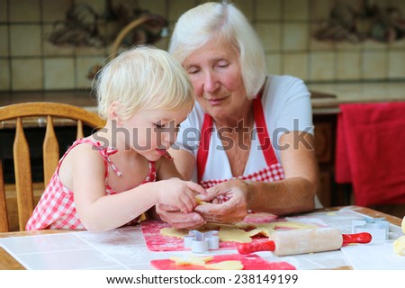 Loving caring grandmother, beautiful senior woman, baking tasty sweet gingerbread xmas cookies together with her granddaughter, cute little toddler girl, sitting in classic traditional wooden kitchen