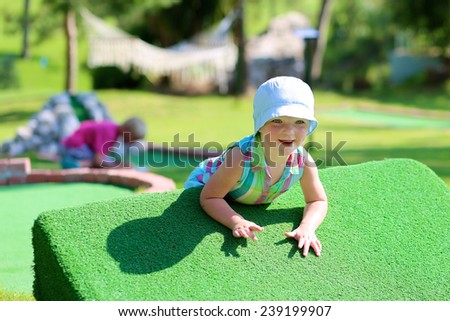Group of happy active children, two brothers, teenage boys, and their little sister, cute toddler girl, playing miniature golf enjoying sunny summer vacation day outdoors in the park