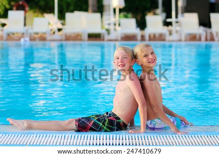 Two happy boys, laughing teenage twin brother, enjoying sunny summer vacation playing in outdoors swimming pool