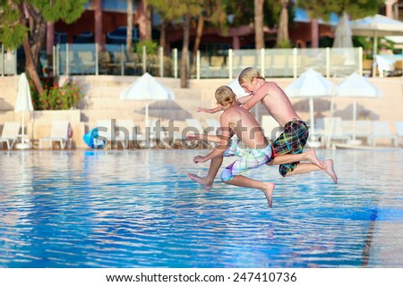Two happy children, twin brothers are jumping into swimming pool at the resort at sunset