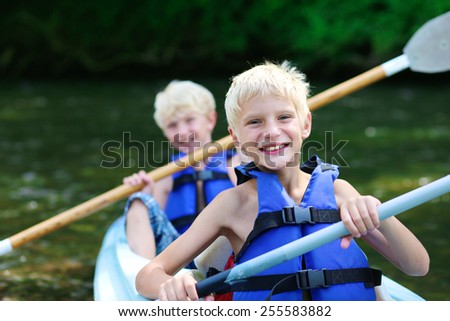 Active happy twin brothers, teenage school boys, having fun together enjoying adventurous experience kayaking on the river on a sunny day during summer vacation