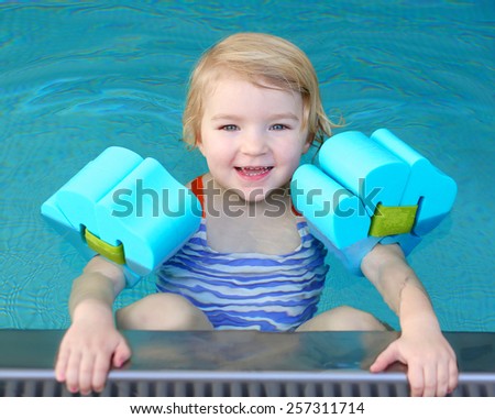 Healthy active little child, laughing blonde toddler girl swimming in the pool learning to float using armbands