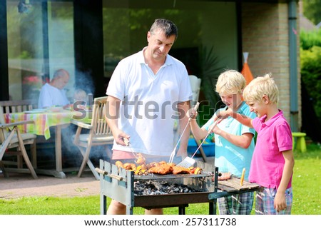 A father with sons, two twin teenage boys cooking meat on barbecue for summer family dinner at the backyard of the house
