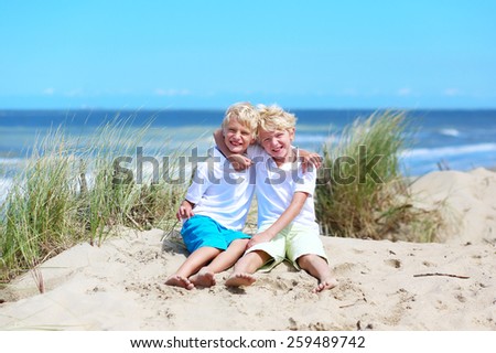 Two happy laughing kids, twin teenager brothers, enjoying summer vacation on sunny day having fun on the beach playing in sandy dunes, North Sea, Belgian coast