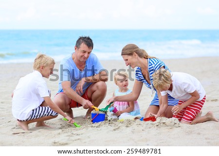 Big happy family of five - young active parents with three kids, twin teenager sons and cute toddler daughter - enjoying summer vacation together building sand castles on the beach at the sea
