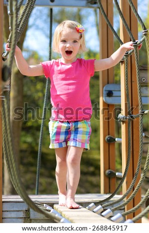 Funny little child, blond sportive toddler girl, having fun climbing on playground in the park on a sunny spring or summer day