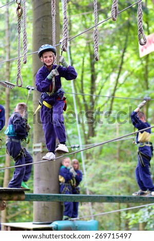 Happy child, healthy teenager school boy enjoying group friends activity in a climbing adventure park on a summer day