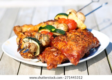 Assorted delicious grilled meat from chicken and pork and various vegetables on white plate on picnic table for family bbq party dinner