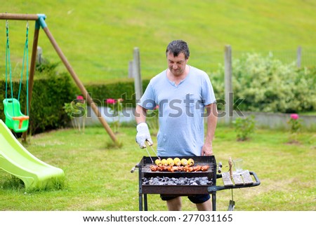 Summertime fun: a man cooking meat on barbecue for summer family dinner at the backyard of the house