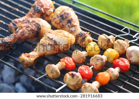 Meat and vegetables on grill. Marinated chicken legs and mushrooms with cherry tomatoes on metal skewers roasted on barbecue grid for summer family dinner