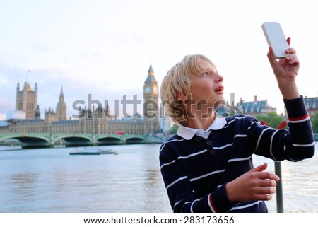 School boy making selfie photo in front of Houses of Parliament, Big Ben and River Thames on a summer evening at sunset, London, UK. Happy caucasian kid enjoying view during family trip to England.