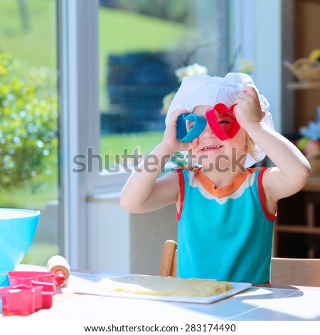 Little happy child, adorable toddler girl in white chef hat helping mother cooking delicious pastry in the kitchen