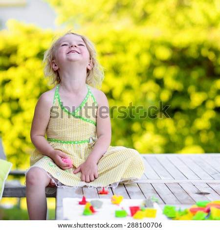 Little girl playing with plasticine and colorful forms. Happy child, adorable toddler girl creating from modeling compound dough, sitting outdoors in the garden on sunny summer day