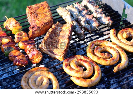 Assorted mixed grill on wooden skewers from chicken meat, lamb and pork, marinated spareribs, sausages and various vegetables roasting on barbecue grid cooked for summer family dinner