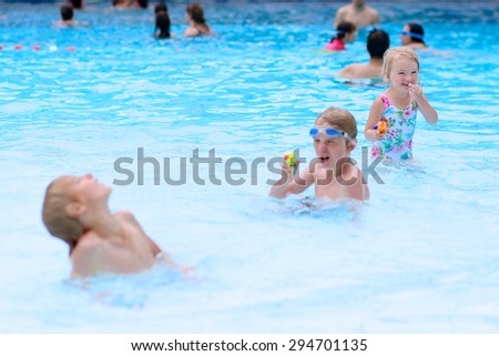 Happy family having fun in recreation swimming pool. Children enjoying day in waterpark during active summer holidays. Kids laughing and playing with waterguns. Selective focus on little girl.