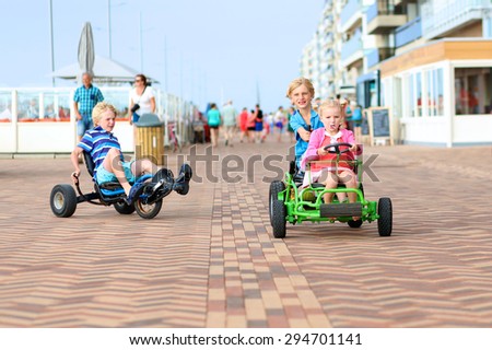Happy kids enjoying active holidays on the beach. Sportive boy riding pedal car together with his cute toddler sister along the promenade on a summer day at sunset.
