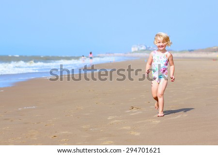 Cute active child playing on sandy beach. Happy little girl enjoying summer holidays on a sunny day. Family with young kids on vacation at the North Sea coast.