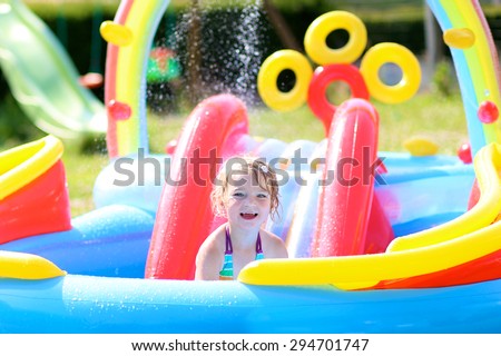 Happy healthy kid having fun in inflatable play centre. Child enjoying summer holidays playing in the pool at the backyard in the garden. Toddler girl relaxing on hot sunny day.