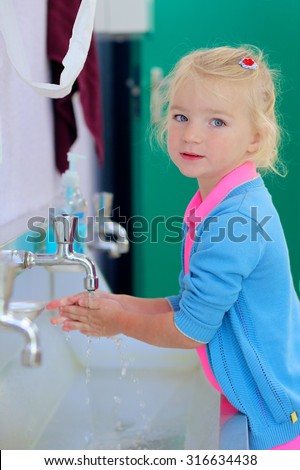 Little toddler girl washing her hands in the bathroom at school or kindergarten