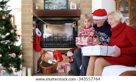 Happy family exchanging christmas gifts in decorated living room with xmas tree and fireplace. Happy loving grandparents giving presents to grandchild.