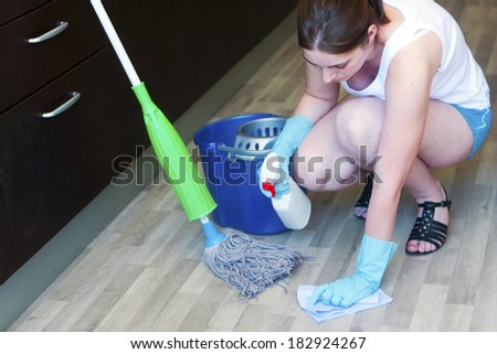 Young girl with cloth and spray kneeling on the floor to clean a spot