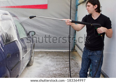 Young man washing car in carwash with high pressure blaster