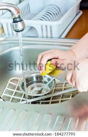 Housewife washing dishes with sponge in kitchen sink