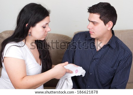 Sad and shocked girl questioning husband about lipstic marks on t-shirt