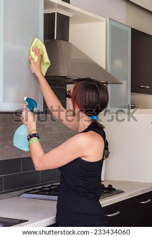 Attractive female teenager cleaning furniture at the kitchen