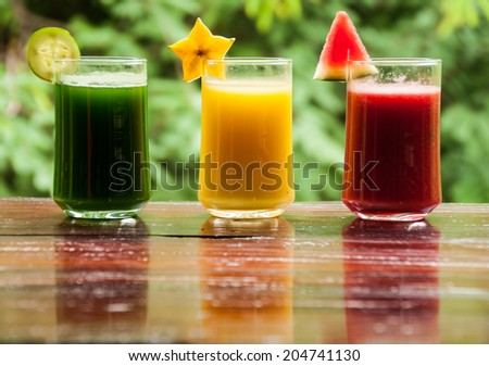 Three of colorful glasses fruit and vegetable juice on wooden table with green background