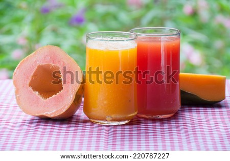 Colorful glasses of papaya juice on table with flower garden background