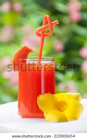 Papaya juice in glass with yellow flower and green background