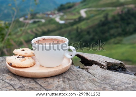 Cup of coffee with cookies on wooden table with mountain road view