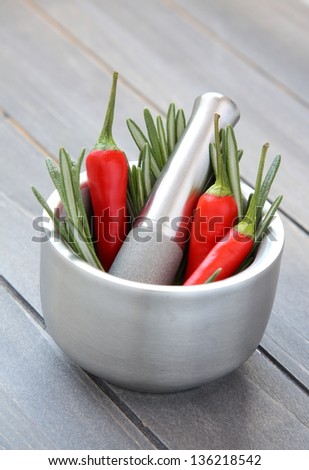 Fresh rosemary herb and red pepper in metal mortar with pestle on wooden background