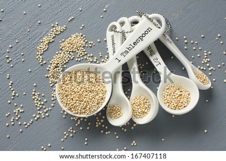 Quinoa grain in porcelain measuring spoons on gray background