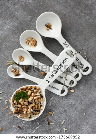 Uncooked multigrain rice in porcelain measuring spoons on wooden background