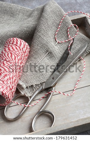 Scissors, spool of thread, needle and sackcloth on wooden tray