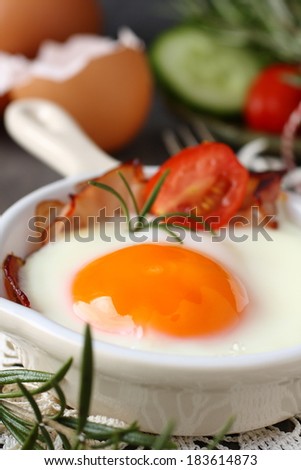 Fried egg with bacon in ceramic pan on wooden background
