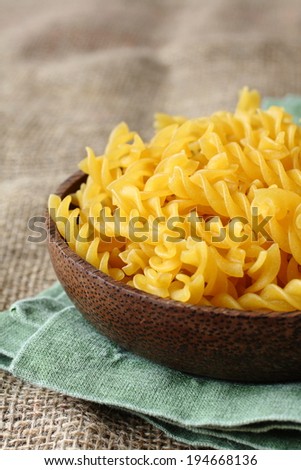 Uncooked gluten free fusilli pasta from blend of corn and rice flour in wooden bowl